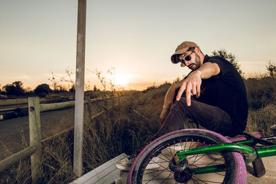 Man looking at bicycle against sky during sunset