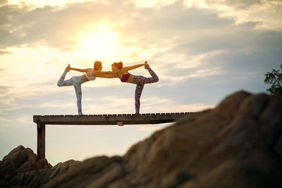 Women exercising on pier against sky during sunset