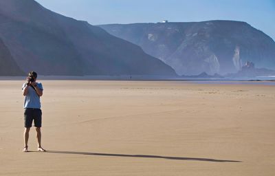 Man photographing through camera while standing on sand at beach