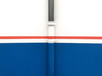 Full frame street shot of blue and white wall with a thin red line crossing and a pipe painted.