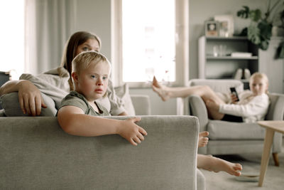 Boy with down syndrome watching tv by mother sitting on sofa at home