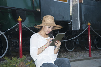 Woman using digital tablet while sitting against train