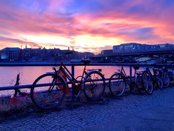 Bicycles by river against sky during sunset
