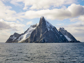 Scenic view of sea by snowcapped mountains against sky