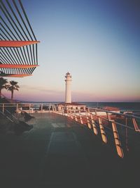 Lighthouse by sea against clear sky during sunset