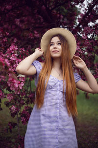 Portrait young beautiful girl teenager in a purple dress and in hat stands blooming pink apple tree