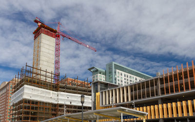 Low angle view of crane by building against sky