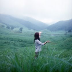 Young woman standing in meadow with raised arms