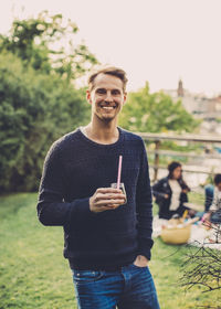 Portrait of happy man holding elderflower drink while having rooftop picnic with friends