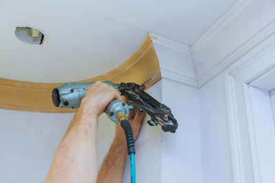 Cropped hands of man using nail gun on wall at home