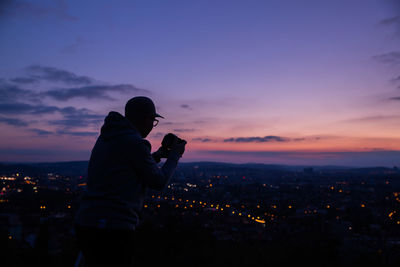 Man photographing cityscape against sky during sunset