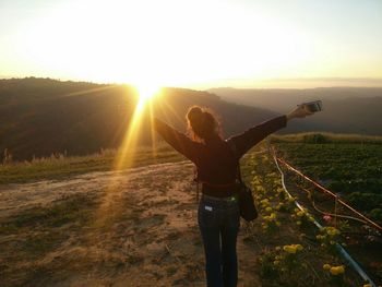 Woman with arms outstretched standing on mountain against sunset sky
