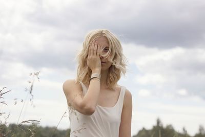 Young woman covering eye with hand against sky