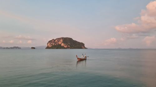 People kayaking in sea against sky during sunset