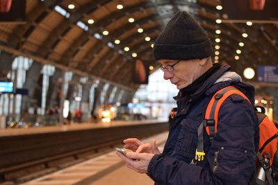 Side view of mature man using mobile phone while standing at railroad station platform