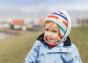 Close-up of cute baby girl in warm clothing looking away while standing on field against sky