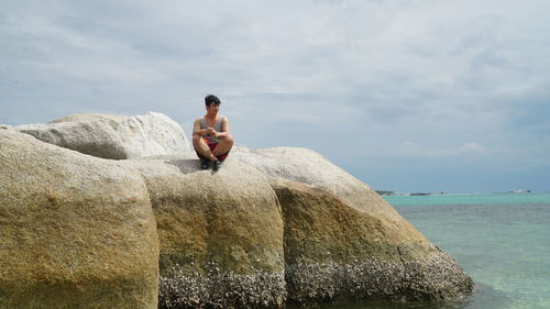 Rear view of woman sitting on rock against sky