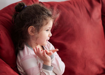 Portrait of a young girl in pajamas sitting on the couch and making faces while watching tv