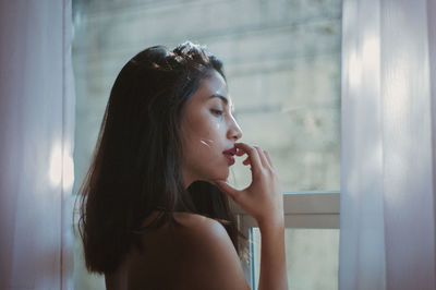 Side view of young woman looking through window