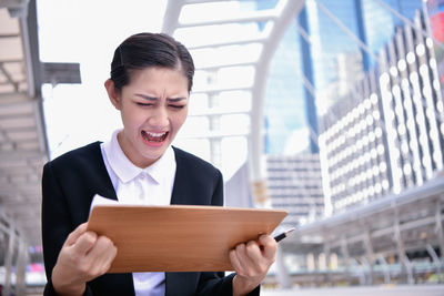 Crying businesswoman holding clipboard while standing in city