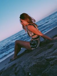 Midsection of woman at beach against sky during sunset