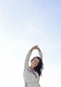 Smiling woman with arms raised standing against clear sky