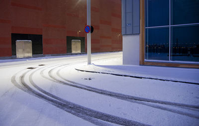 Snow covered road by building in city at night