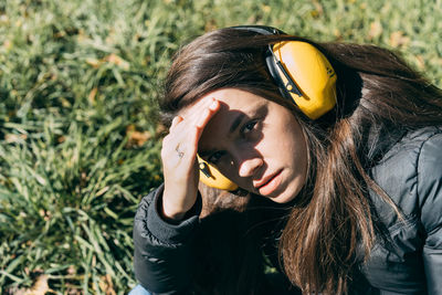 Close-up portrait of young woman wearing headphone on field during sunny day
