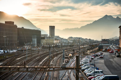 Railroad tracks by buildings against sky during sunset