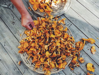 Cropped hand of man holding mushrooms in wicker basket on wooden table