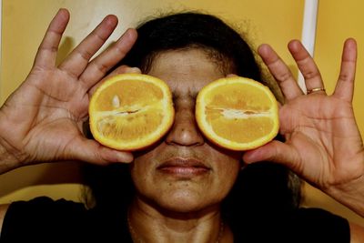 Close-up of mature woman covering eyes with oranges 
