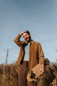 Young man holding camera while standing on field against sky