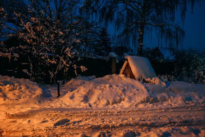 Snow covered field by treesand a little house against sky at night