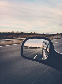 Close-up of side-view mirror against sky