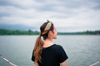 Young woman standing by lake against sky