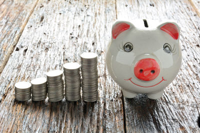 High angle view of coins with piggy bank on wooden table