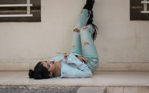 Fashionable young woman lying on floor with feet up against wall