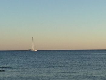 Sailboat sailing on sea against clear sky during sunset