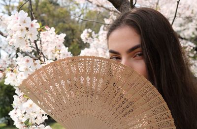 Portrait of teenage girl with folding fan against flowering trees at park