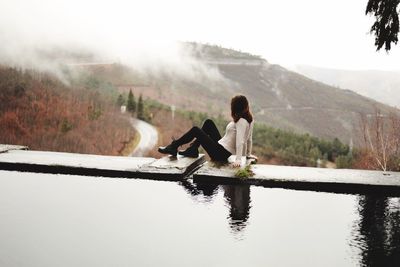 Woman sitting at infinity pool against mountains