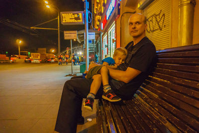 Father with son sleeping on lap at bench during night