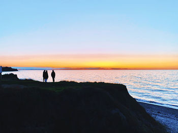 Silhouette people on beach against sky during sunset