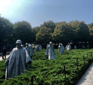 Rear view of people sculpture in cemetery against sky