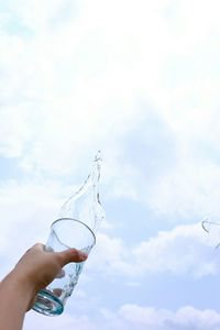 Low angle view of hand holding drink against sky
