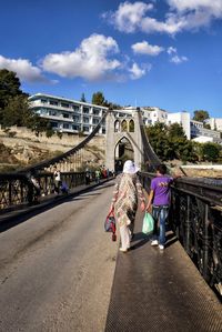 Rear view of people walking on bridge against sky