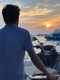 Rear view of man looking at sea against sunset sky