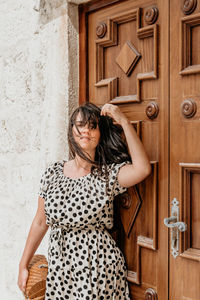 Portrait of attractive young woman in polka dot dress. standing in front of brown wooden door.