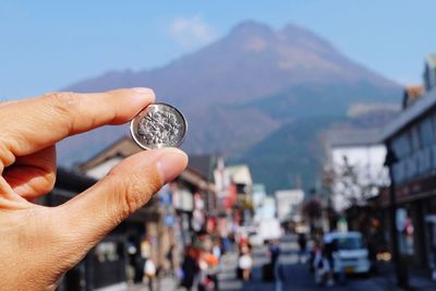 Cropped hand holding coin against mountain