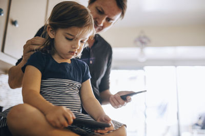 Daughter using phone while father standing in kitchen