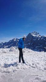 Full length side view of woman standing on snow against mountain and blue sky